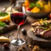 Glas rode wijn naast gourmetgerechten met kaas, kruiden en gegrild vlees op houten tafel in warm licht
